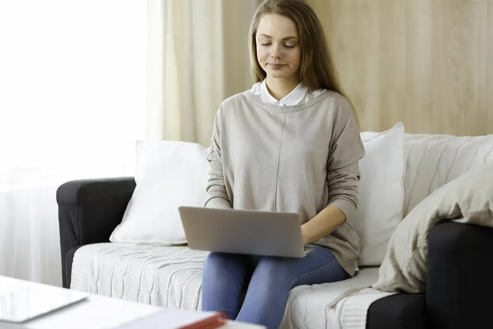 Una mujer sentada en un sofá con el portátil en las piernas hace uso de la consulta de psicología online